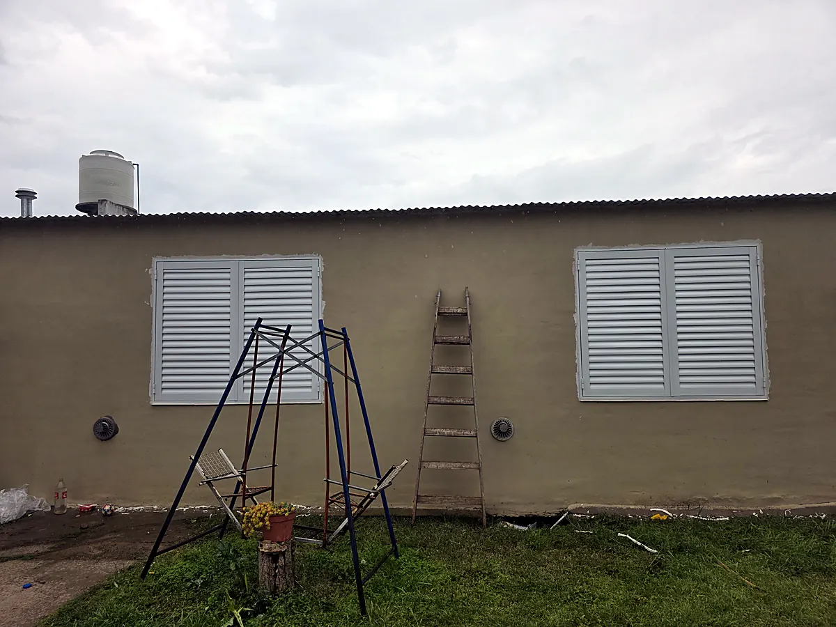 Dos ventanas con postigos de aluminio en un patio